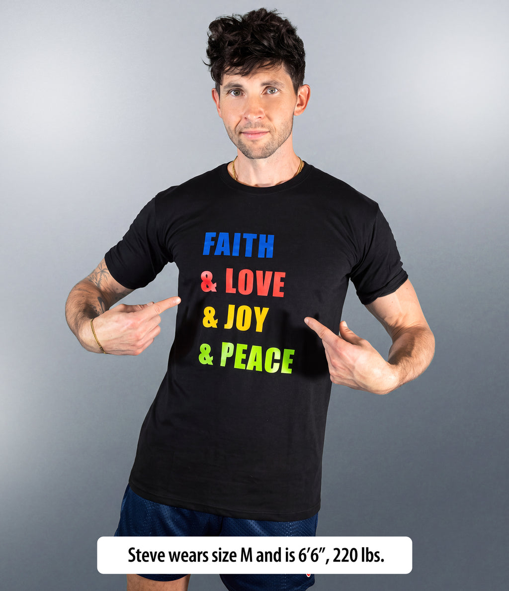 A man wearing a black graphic t-shirt with the words 'FAITH & LOVE & JOY & PEACE' printed in blue, red, yellow, and green. He is pointing at the text on his chest.